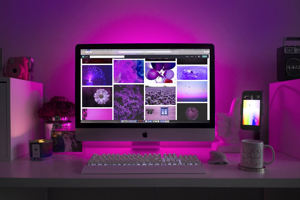 Modern desk setup with neon lighting and a desktop computer displaying colorful images.